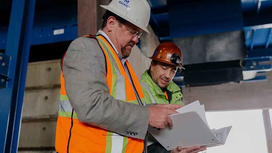 two men look at a binder in an industrial setting