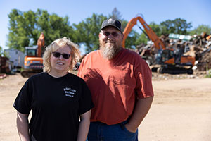 a woman and man stand beside one another in a scrap yard