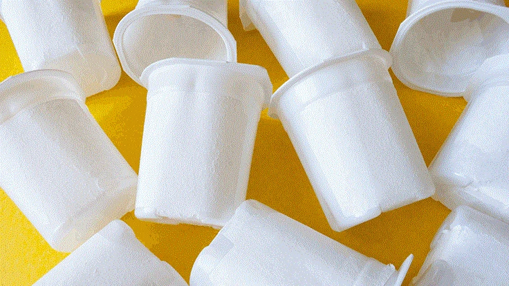 empty white yogurt conatiners yellow background