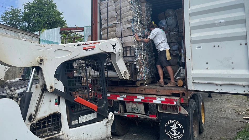 a skid steer loads bales intoa shipping container on a truck