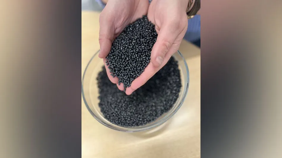 a person holds black abs plastic pellets in his hands over a bowl filled with the pellets