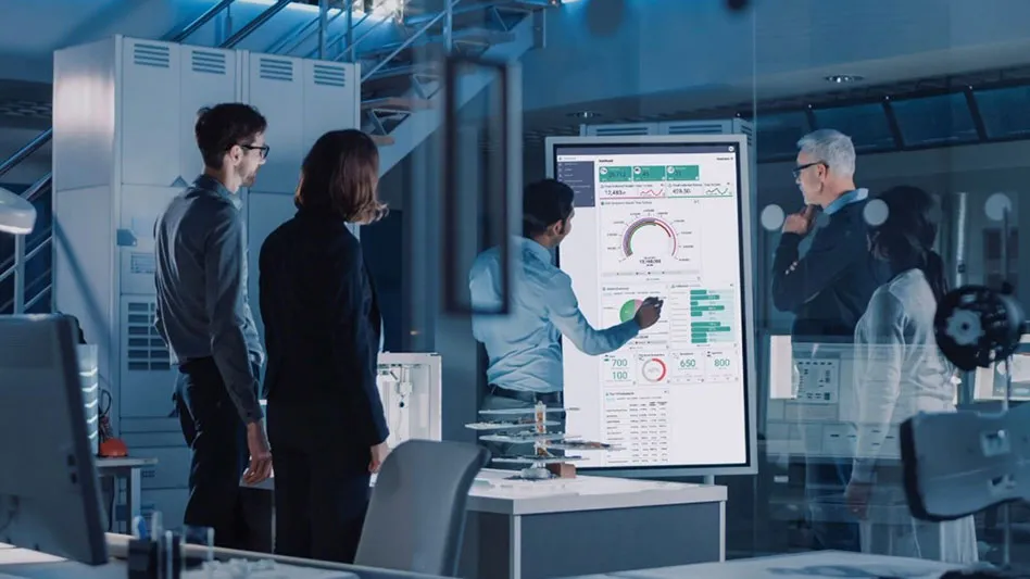four people stand before a screen with charts and graphs on it