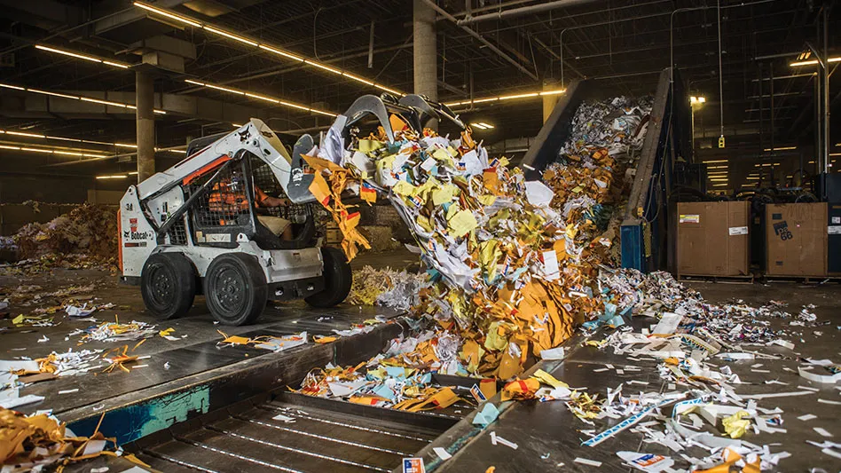 a skid-steer pushes paper onto a conveyor belt in the floor