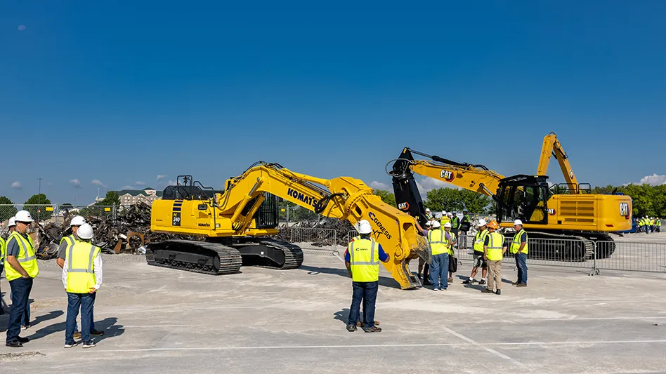 two pieces of heavy equipment and people in yellow work vests