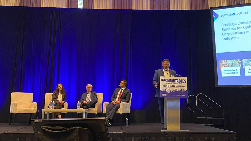 a woman and two men are seated in chairs on a stage while a man presents at a podium