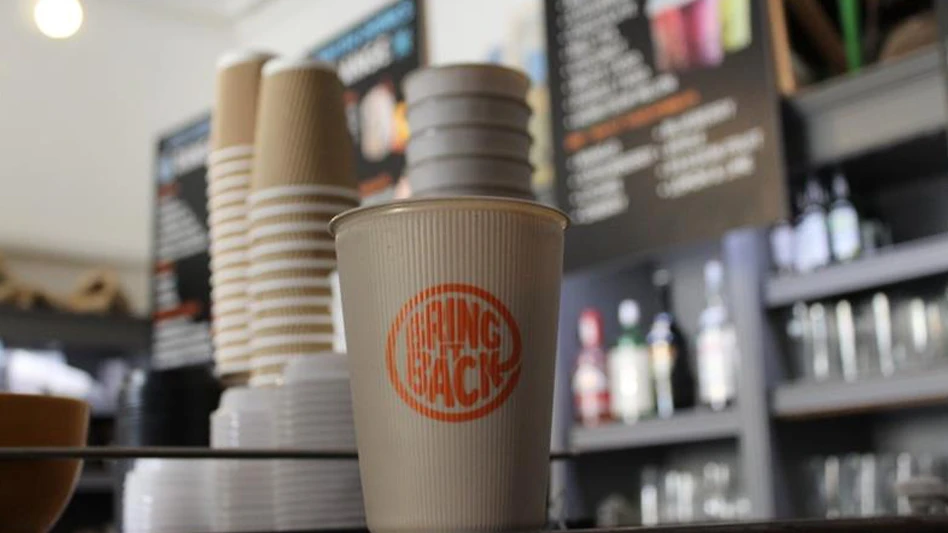 A Bring It Back reusable cup sitting on a cafe counter.