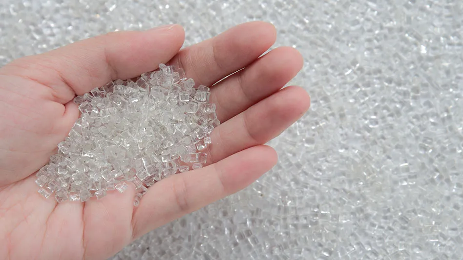 a hand holding clear PET pellets above an expanse of clear PET pellets
