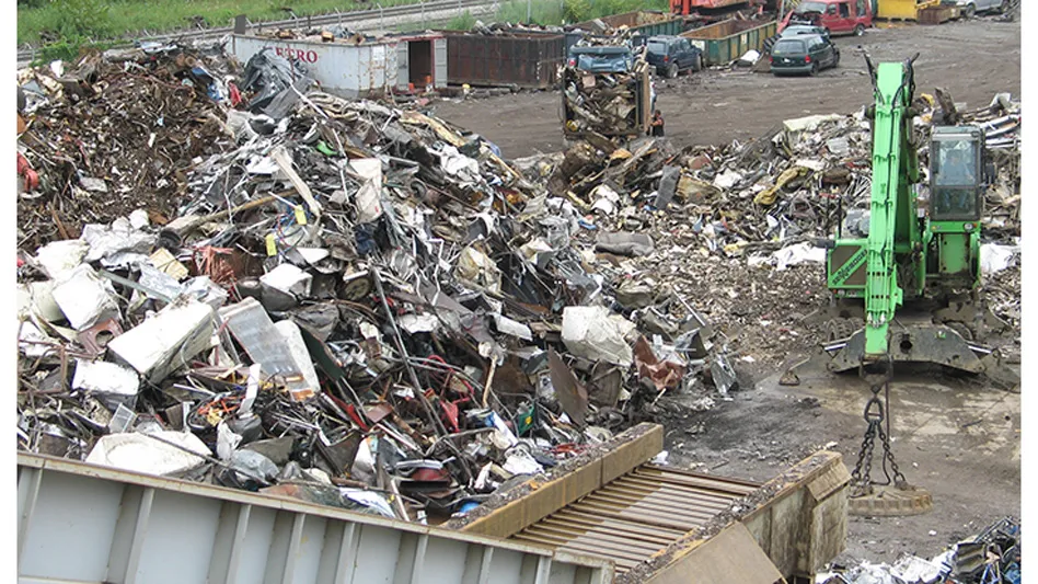 a material handler sits beside a pile of ferrous scrap and the infeed conveyor to an auto shredder