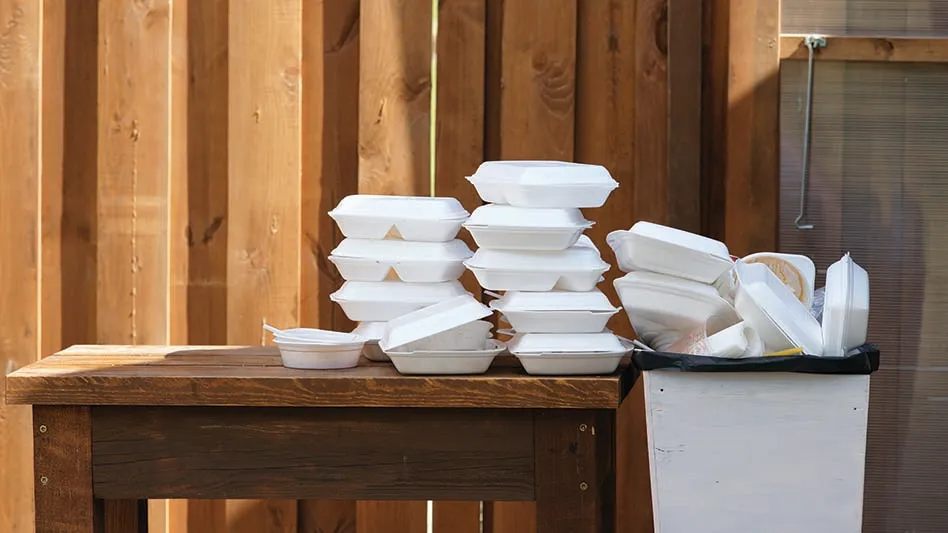 A pile of plastic foam food containers sitting on a table, headed for a trash can.