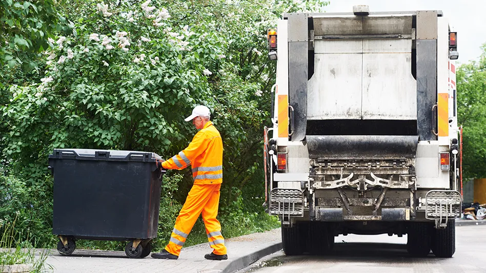 man in orange work clothes leads collection cart to waste truck