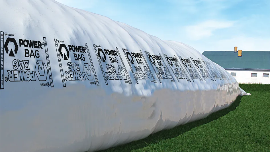 A large, white AAG agricultural bag made with performance polyethylene developed by ExxonMobil sitting on grass in front of a building.