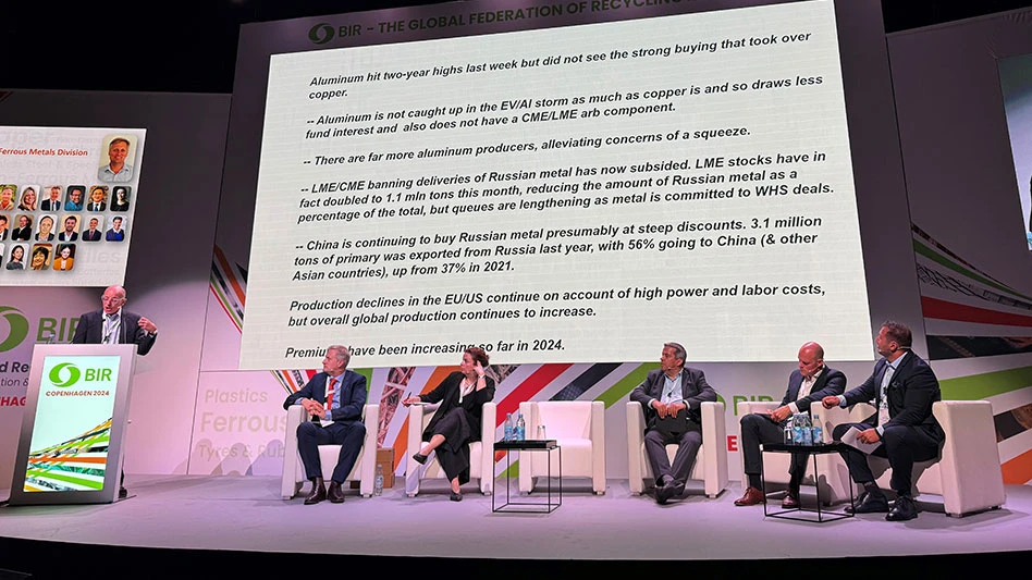 a man talks at a podium while four men and a woman looks on