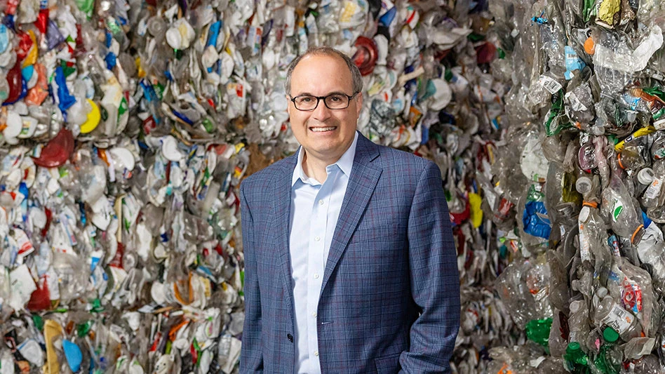 a smiling balding man with glasses stands in front of bales of recyclables