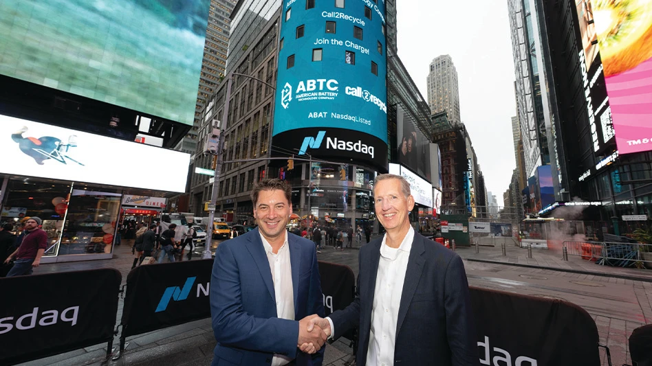 Two men shake hands in front of a large Nasdaq sign in New York City.