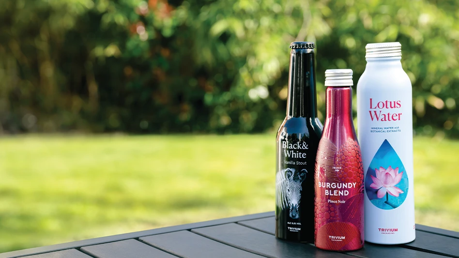 Three beverage bottles of different sizes and colors sit on a wooden table outdoors.