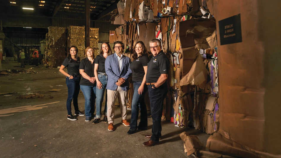 A group of men and women stand in front of bales of cardboard.