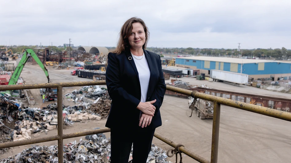 A woman poses in front of a scrapyard.