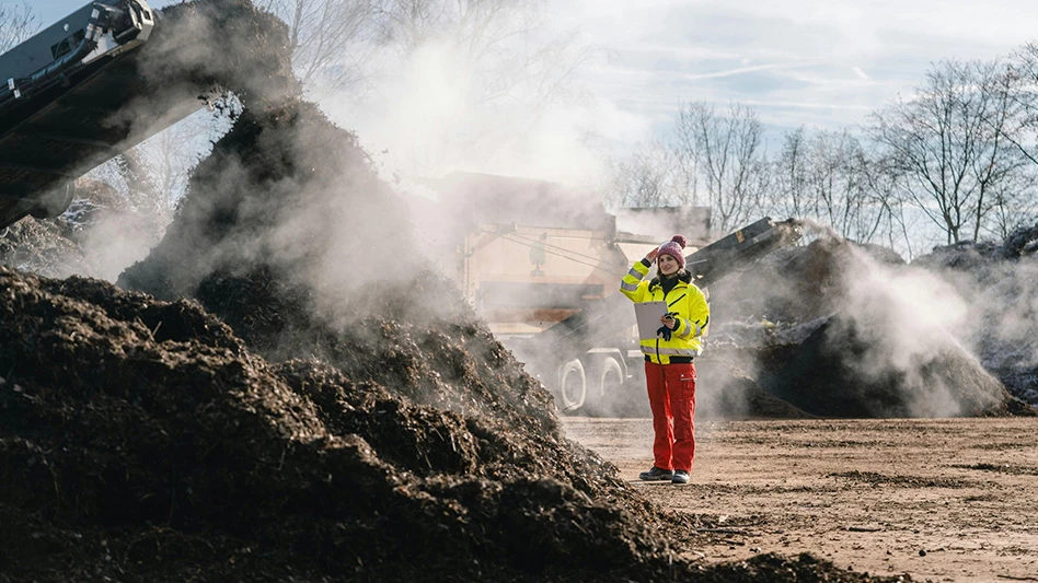 Person stands by pile of compost.