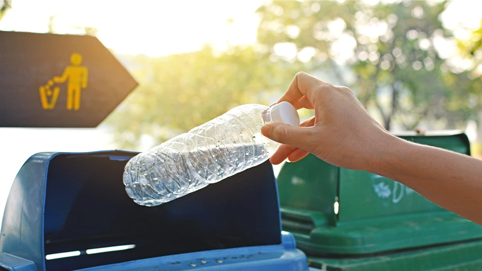 person putting plastic water bottle in blue recycling bin