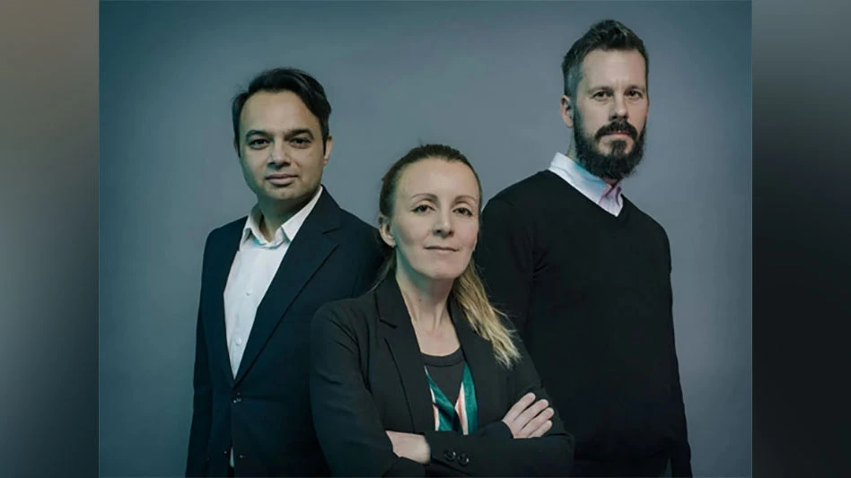 a blonde woman with her arms crossed stands surrounded by two men