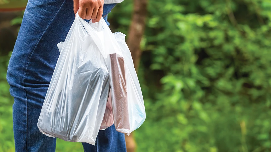 A person walks outside while carrying plastic grocery bags.