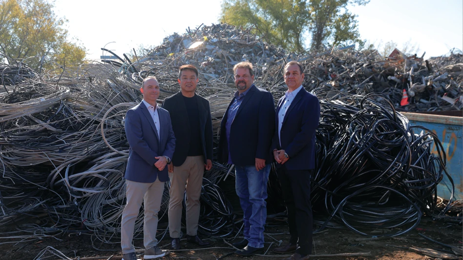 Four men stand in front of a pile of metal scrap.