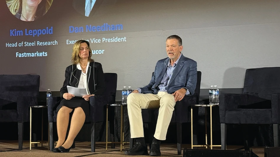 A man and woman talk while sitting on a stage at a conference.