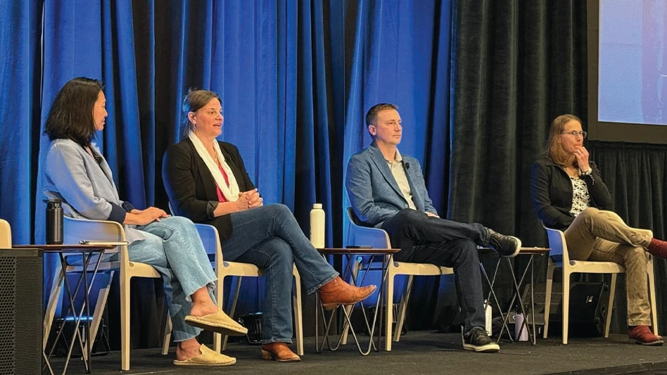 four people sit on a stage during a conference.