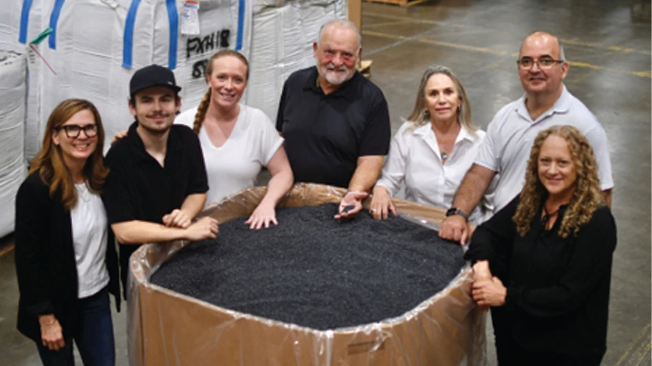 Men and women stand around a container of processed plastic.