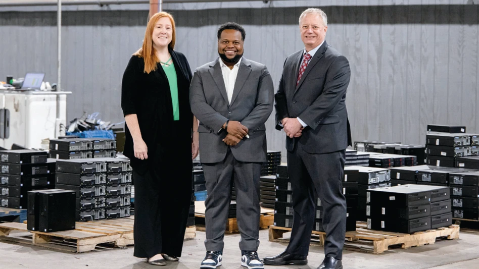 Three people pose for a photo inside an electronics recycling facility.