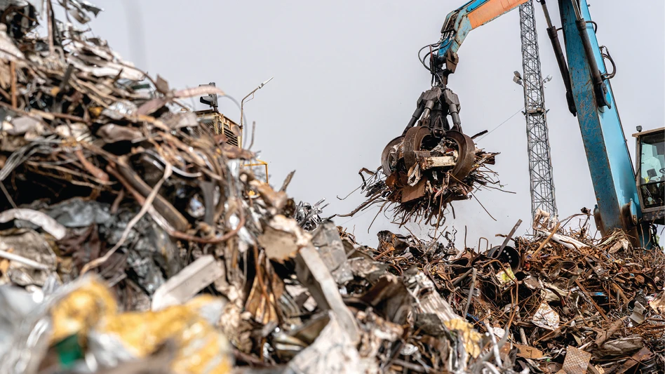 A material handler lifts scrap metal from a pile at a scrapyard.